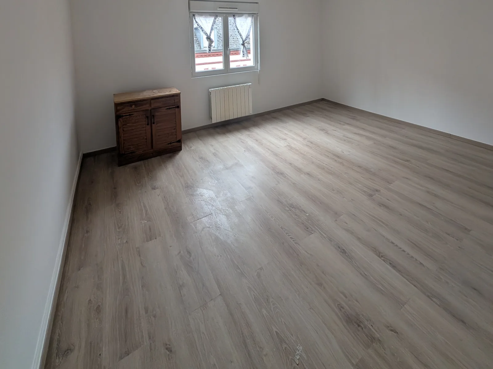 Pièce après rénovation : murs et plafond peints en blanc, sol stratifié posé